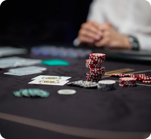 Póker zsetonok és kártyák halmai egy kaszinó asztalon, a háttérben egy elmosódott játékos a játék közben.